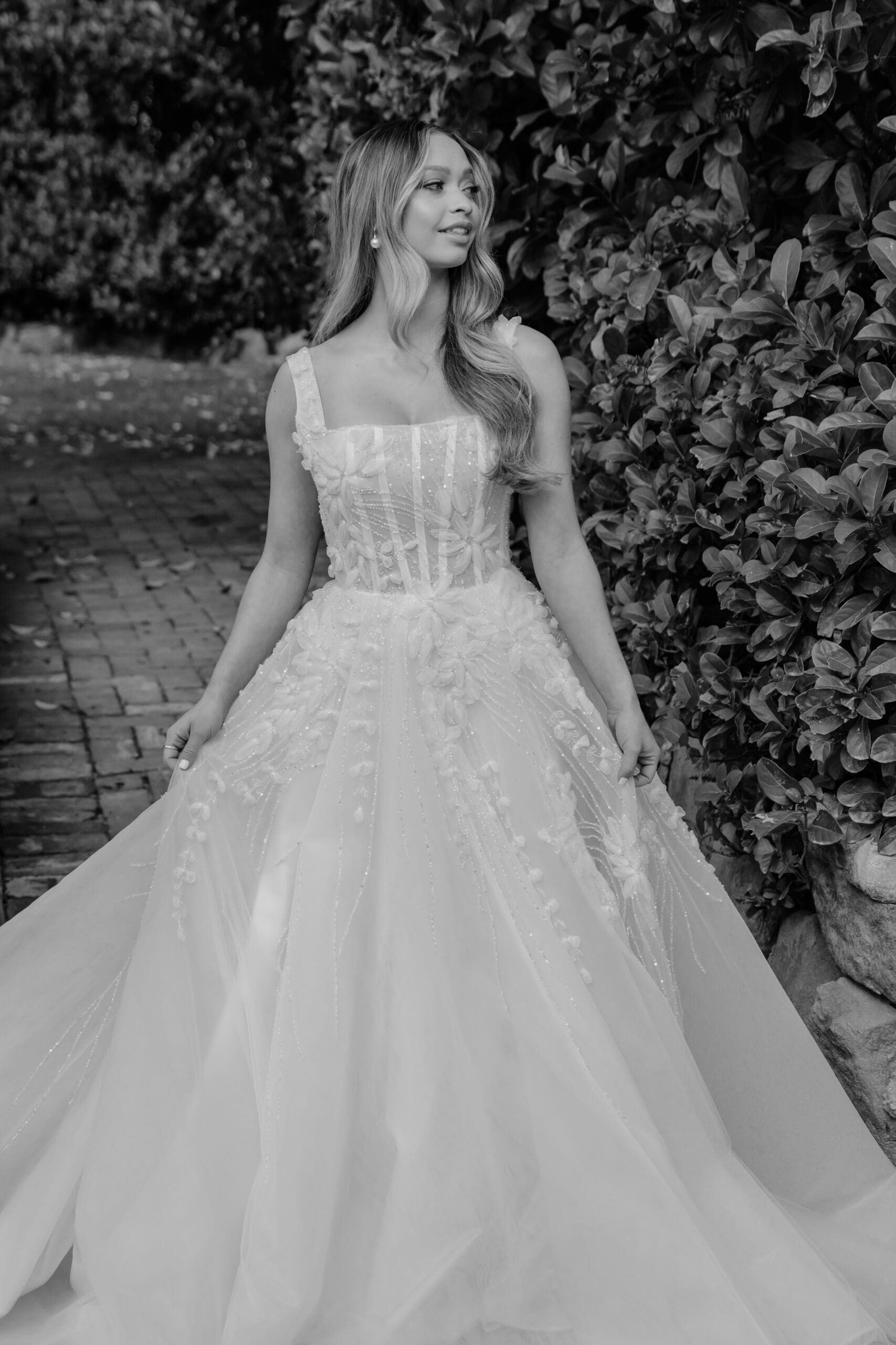 Bride standing in a garden wearing a detailed wedding gown with a full skirt.
