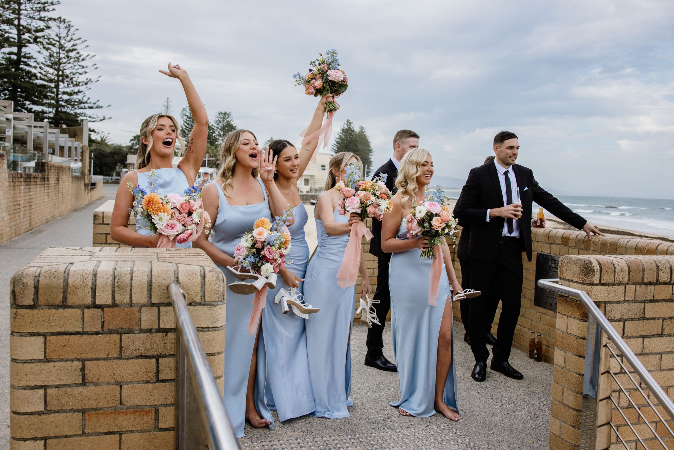 Bridal party celebrating together outdoors with bridesmaids raising their bouquets.